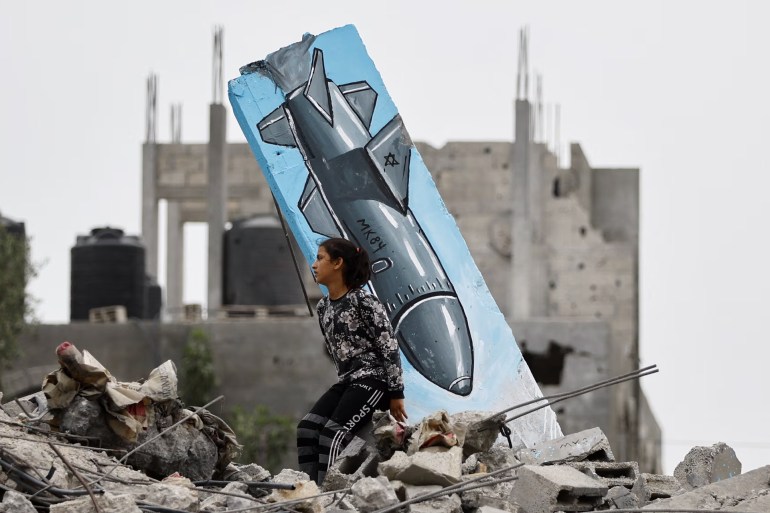فتاة فلسطينية تجلس على أنقاض منزل مدمر، بجانب رسومات لصاروخ لحسين أبو صادق. صورة فوتوغرافية: (رويترز)